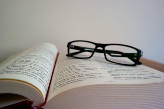 An open book with eyeglasses resting on top, symbolizing learning and education.